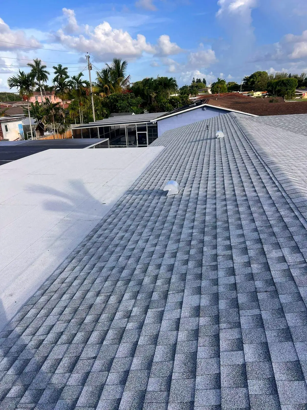Finished gray shingle roof beside a white flat roof section